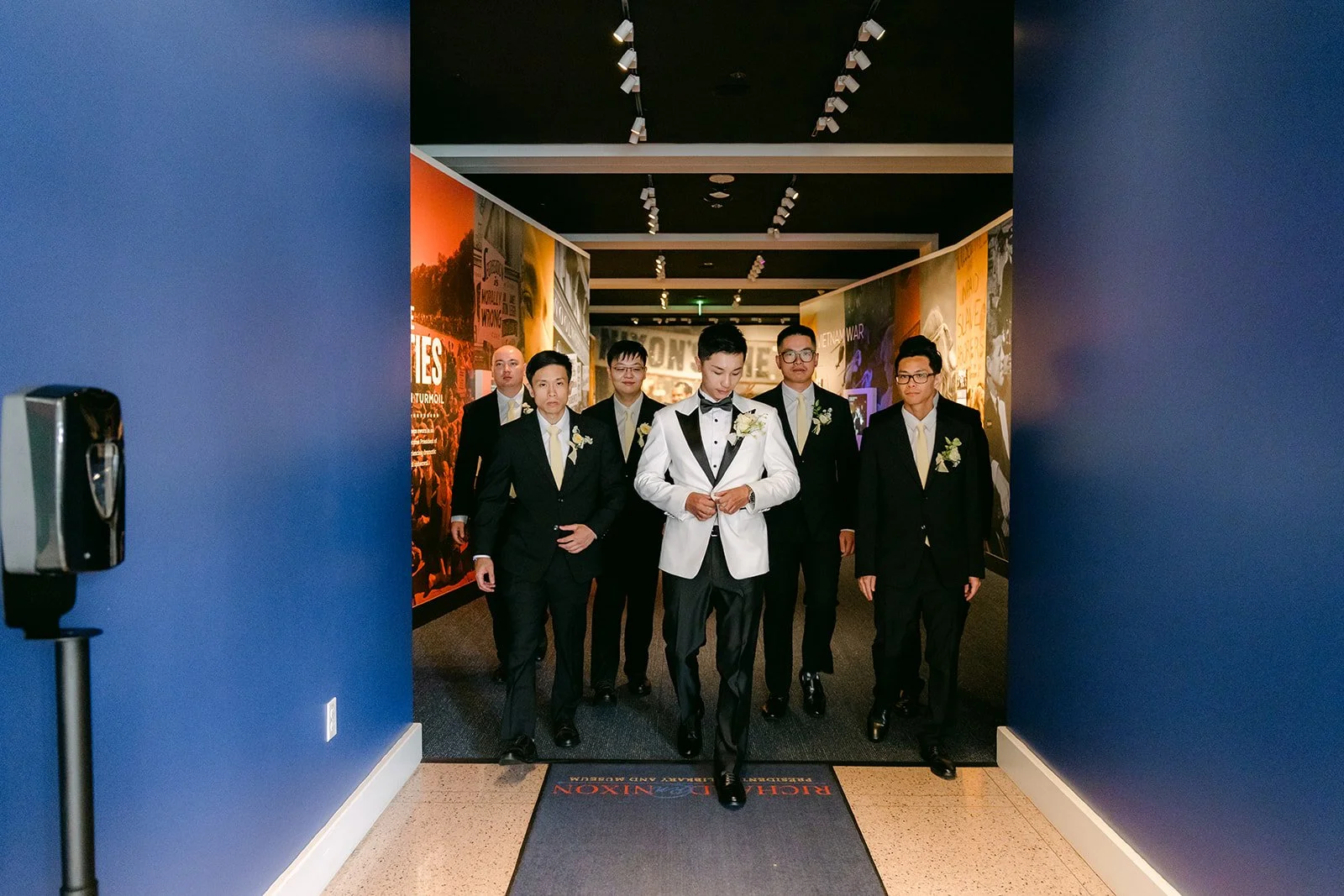 Ryan and his groomsmen walking out of a blue hallway at the Nixon Library.