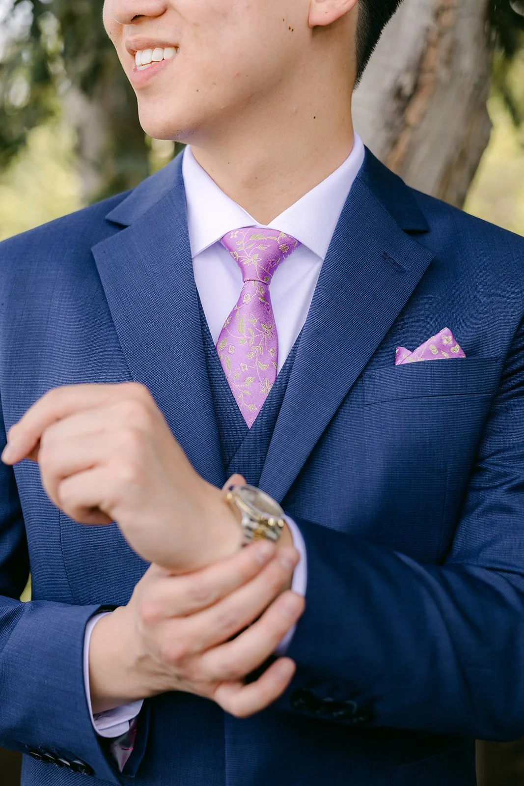 Elijah fastening his cufflinks in his navy suit.