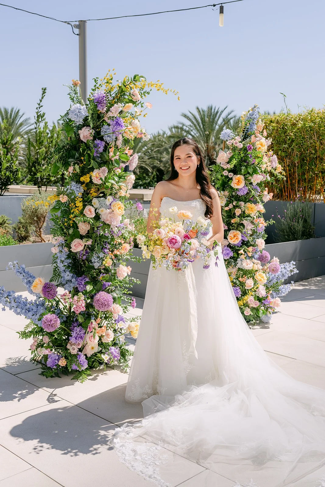 Bride standing in front of a pastel floral arch in the Serenity Garden