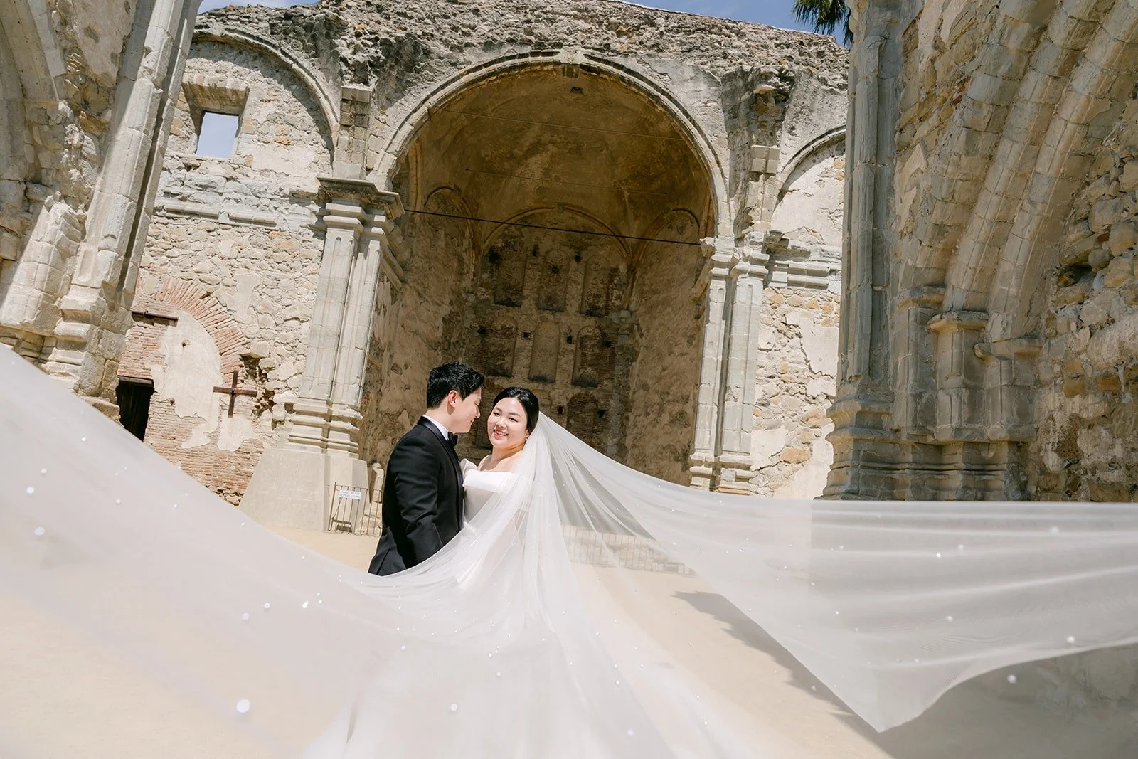 Chorok and Min Soo kissing as her veil floats in front of the stone ruins at Mission San Juan Capistrano
