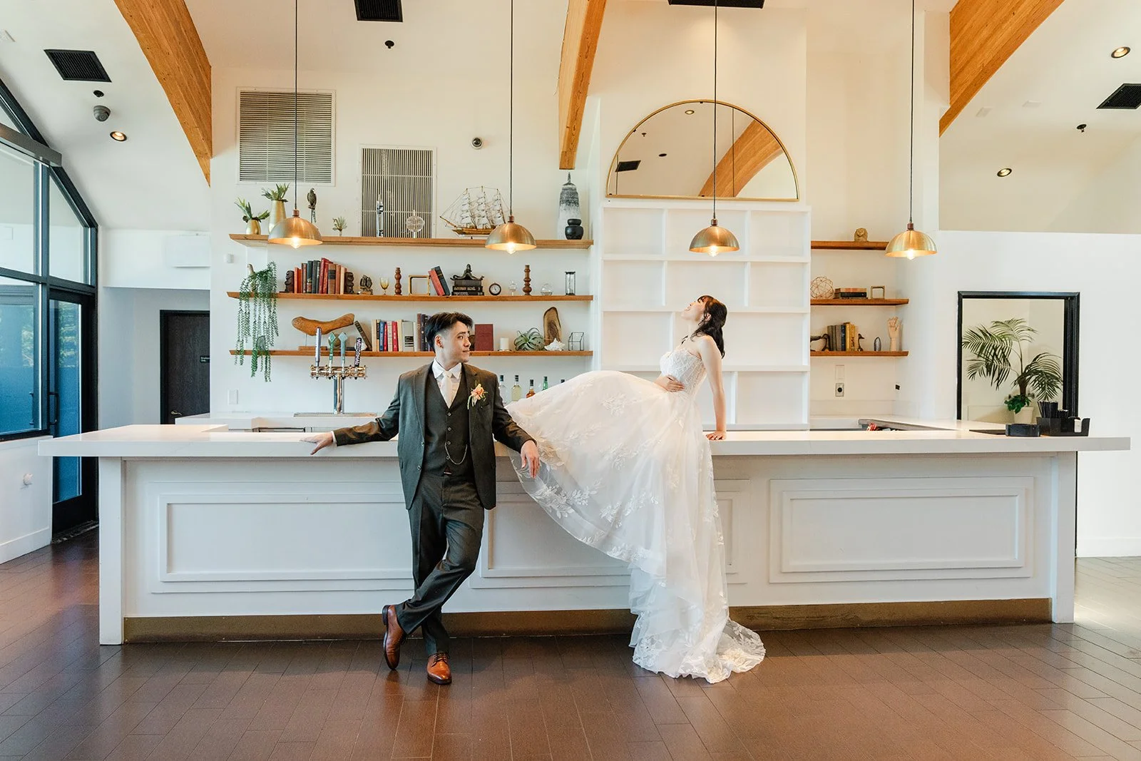 Wide view of the couple by the bar and arched shelves at The Colony House