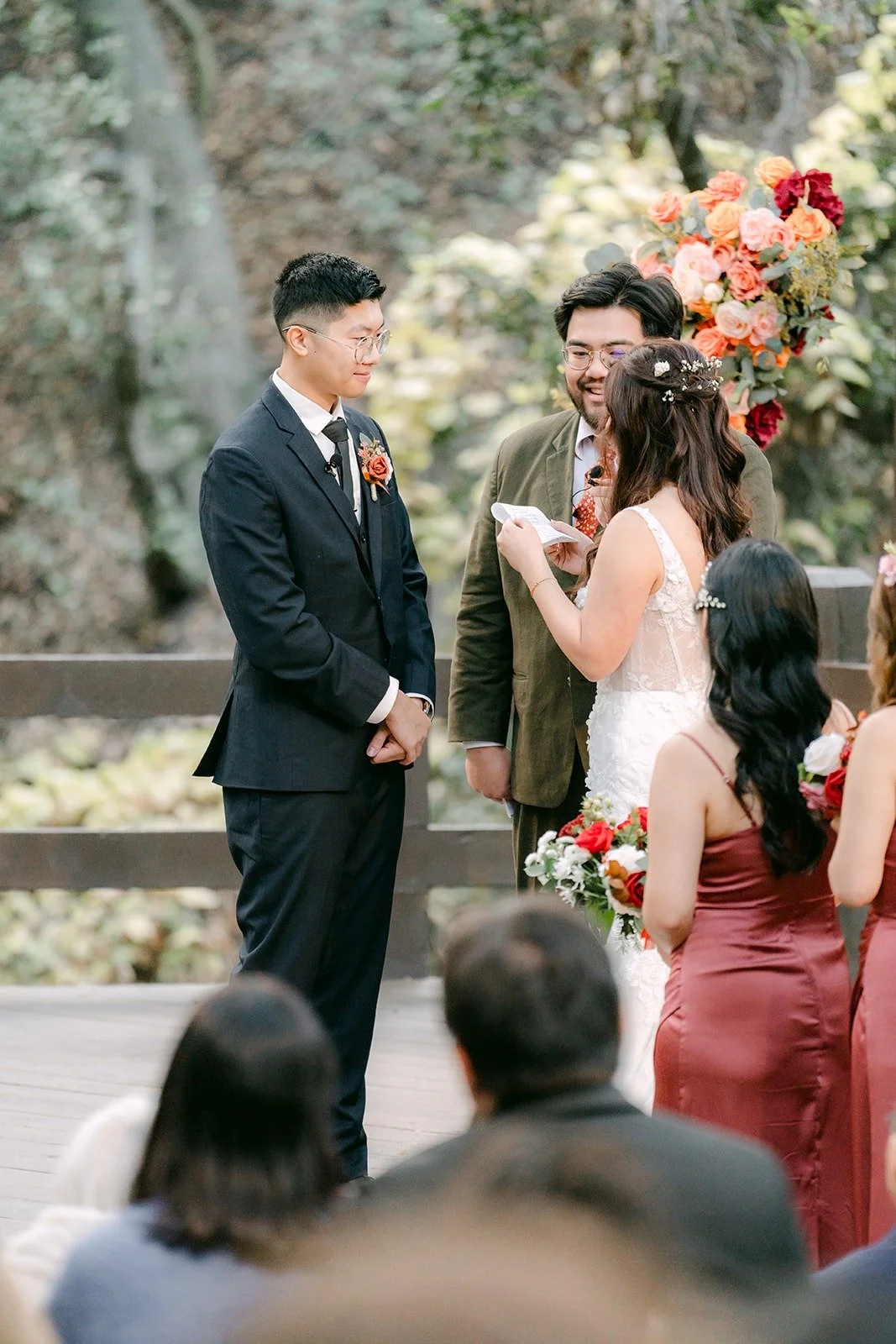 Shayna and Robert hold hands before the officiant at the floral arch