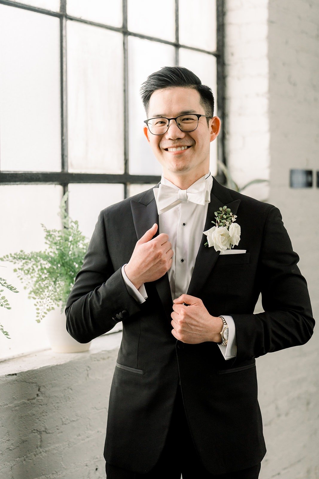 Alex smiles as he buttons his jacket by the windows
