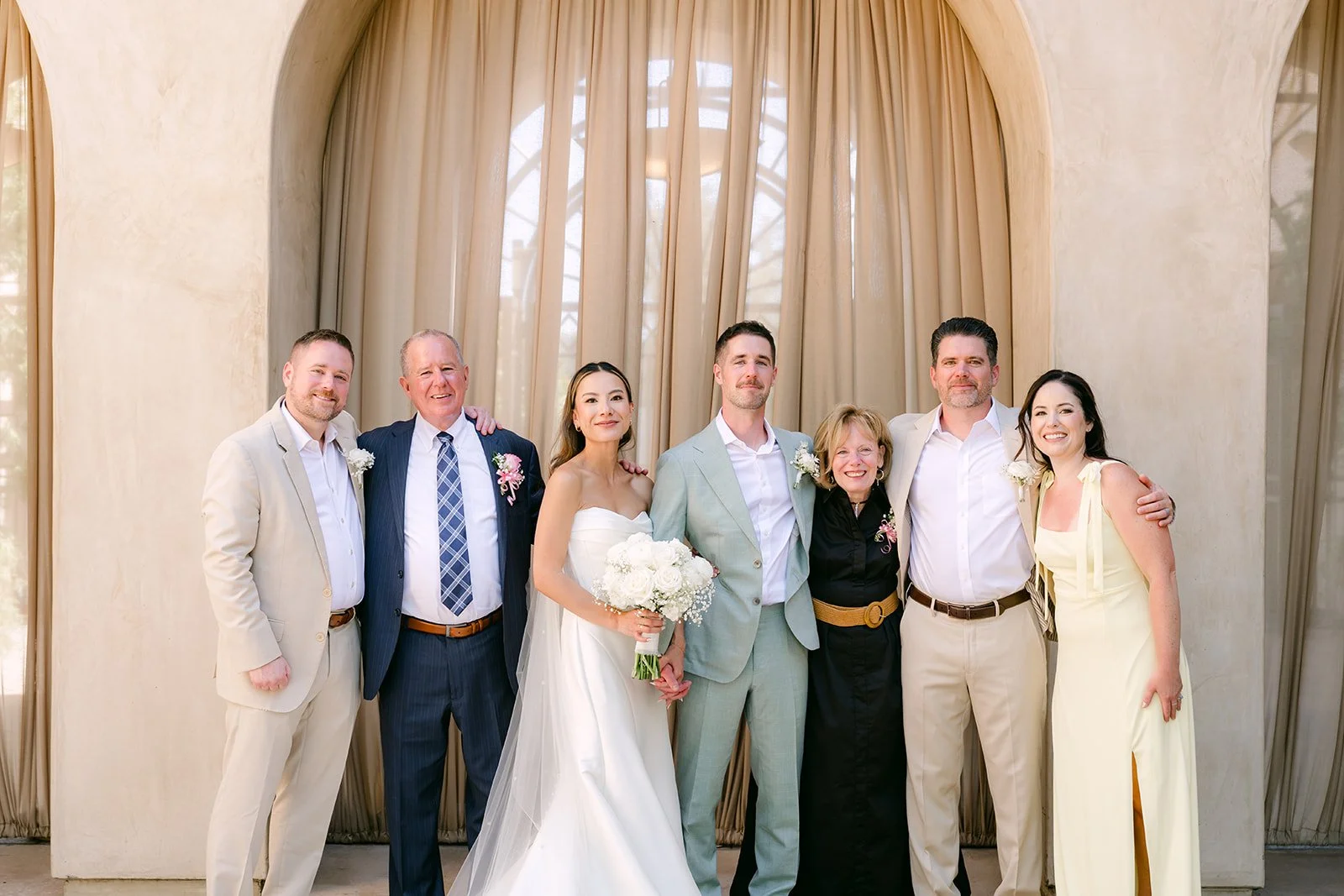 Bride and groom with family in front of a draped arch