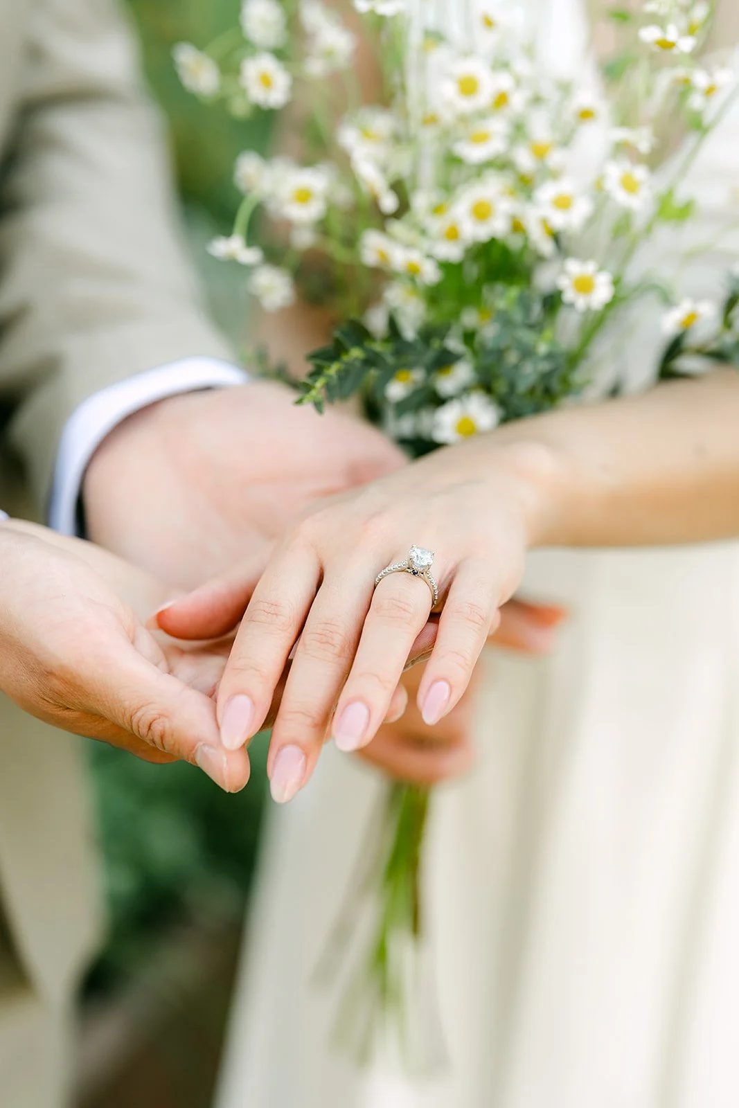 Kim's hand and engagement ring resting in Vincent's beside her bouquet.