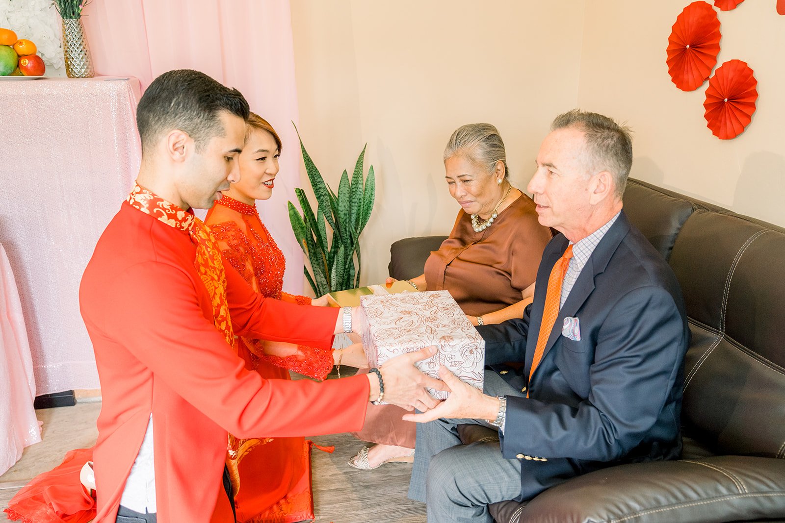 A groom presenting tea to grandparents seated on the sofa.