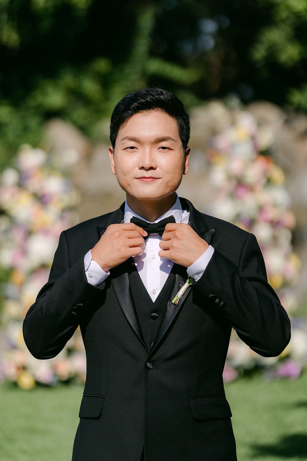 Eunsang adjusting his bow tie in front of the ceremony florals, photographed by One and Only Production