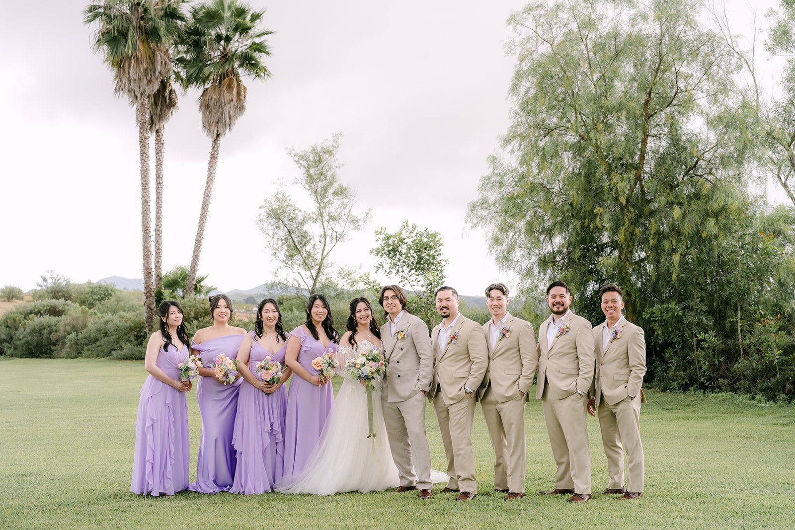 Full wedding party on the lawn with palm trees behind them