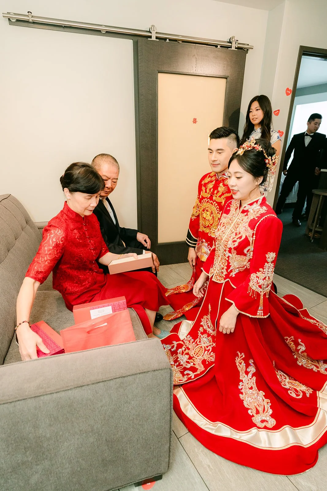 A bride in her qun kwa kneeling on a red cushion to serve tea.