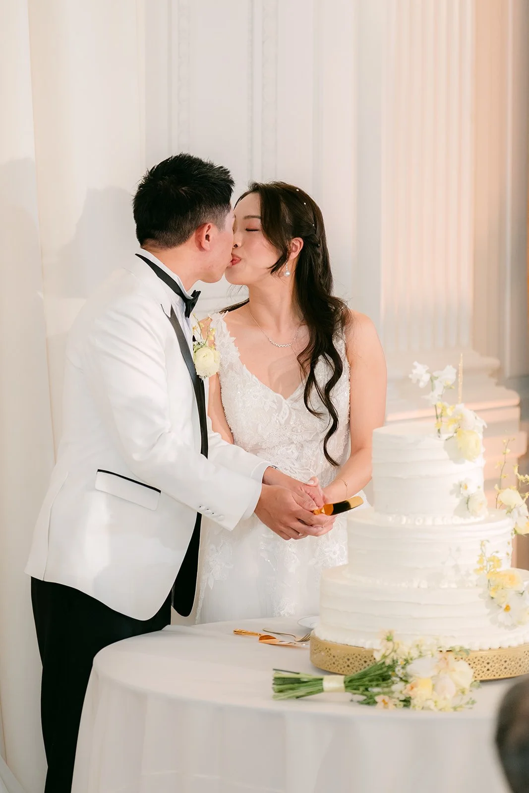 Jenny and Ryan kissing beside their white wedding cake.