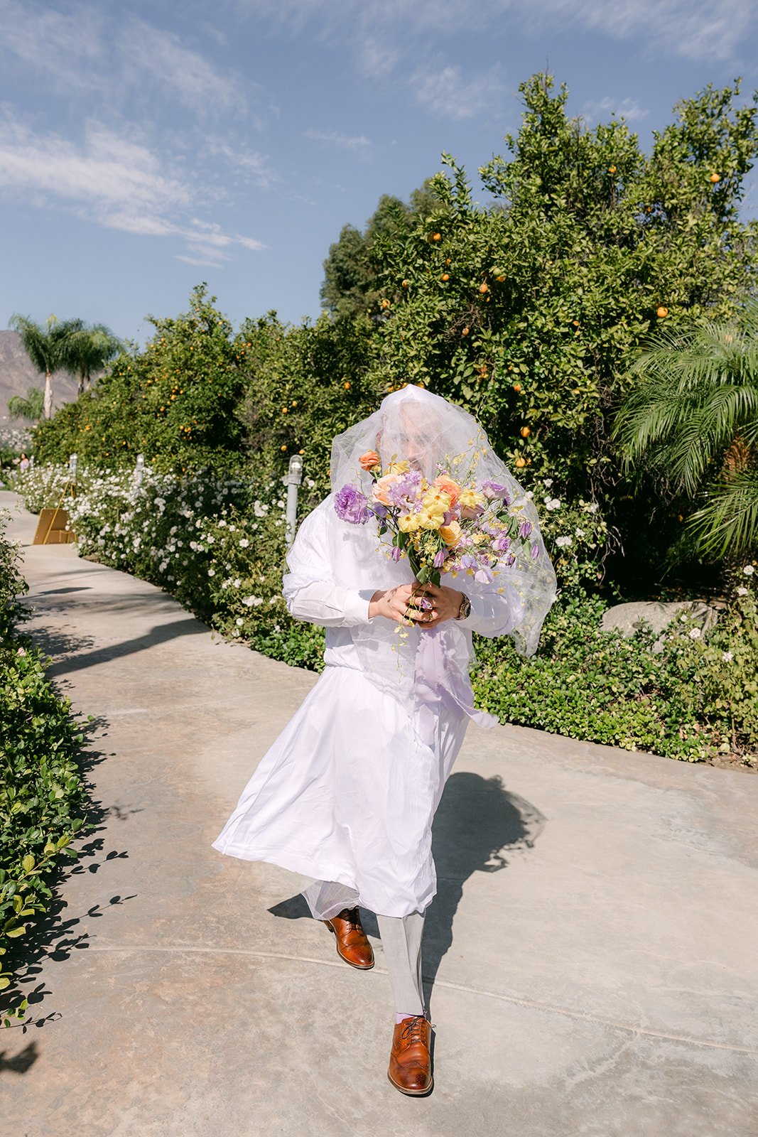 A groomsman in a veil and white dress walking up for a prank first look.