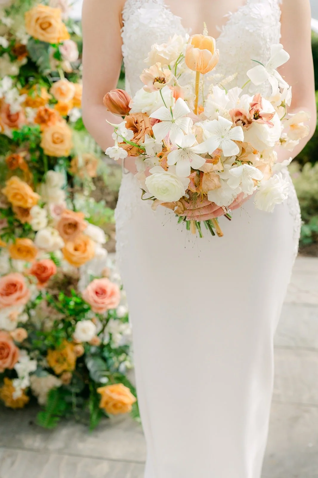 Angela holding her bouquet beside a tall arrangement of peach florals