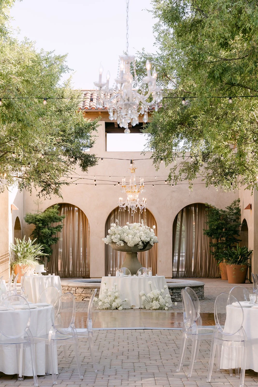 Reception tables with white linens under a chandelier at Serra Plaza