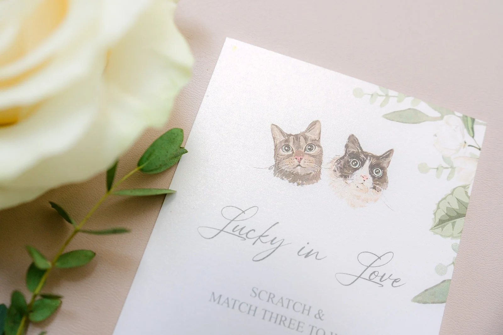 Tin's earrings resting on the invitation beside a cream rose
