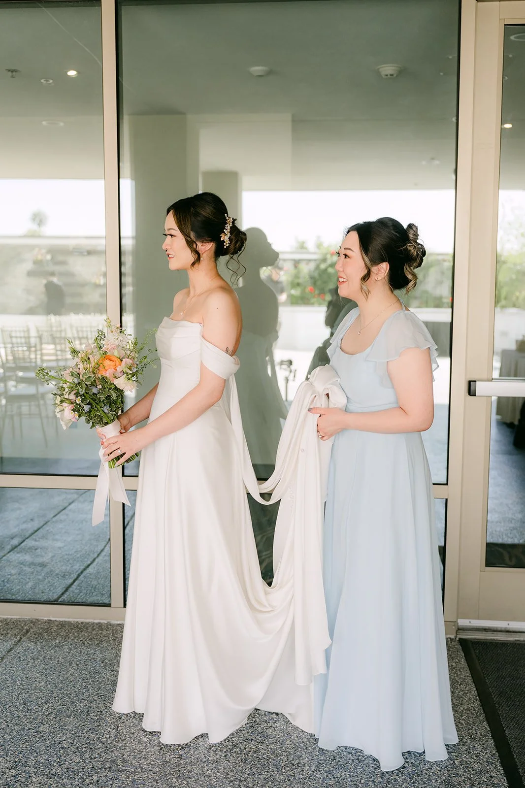 Amanda and a bridesmaid in light blue by the window, photographed by One and Only Production.