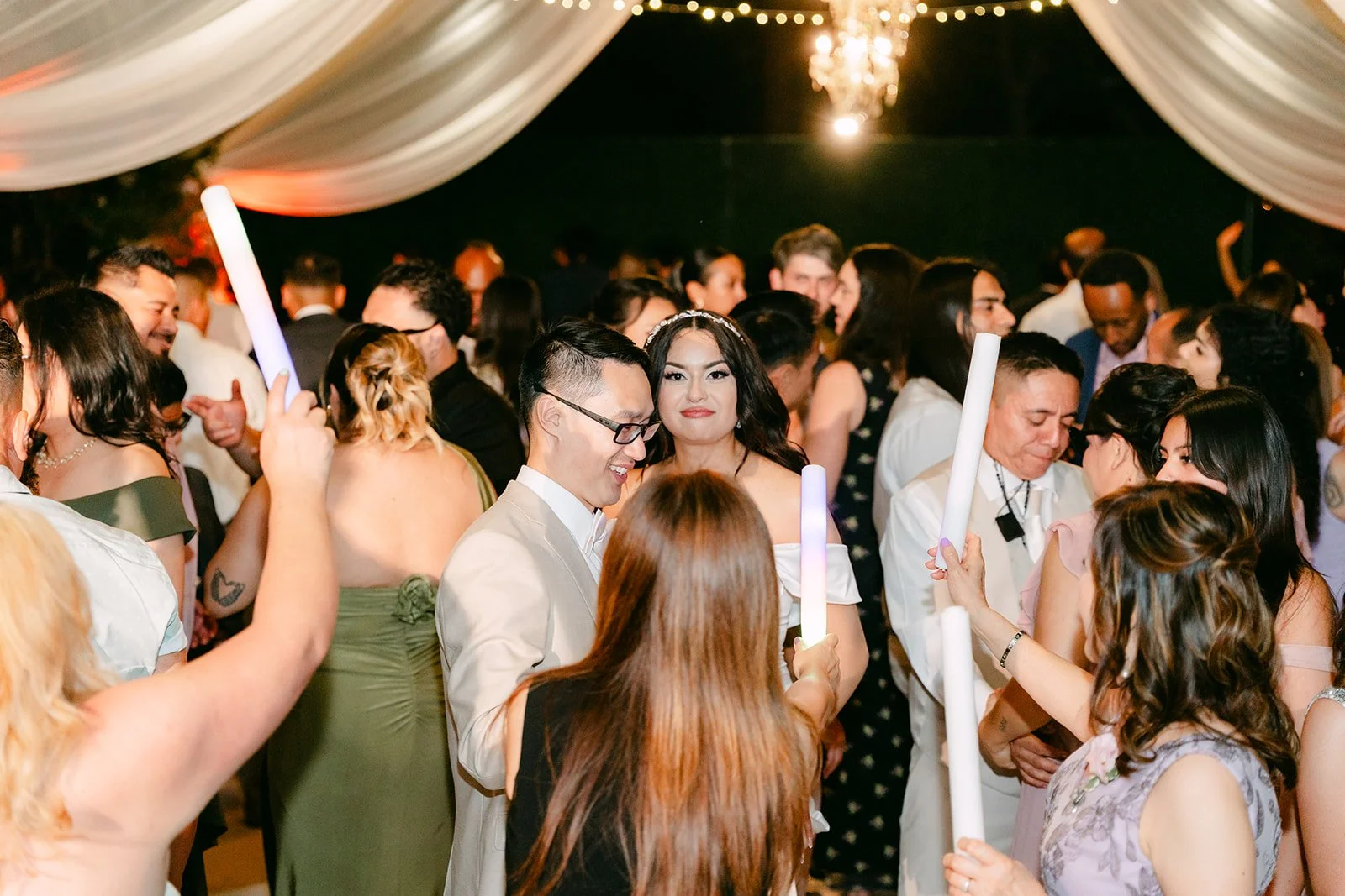 Guests dancing with glow sticks under the chandeliers.