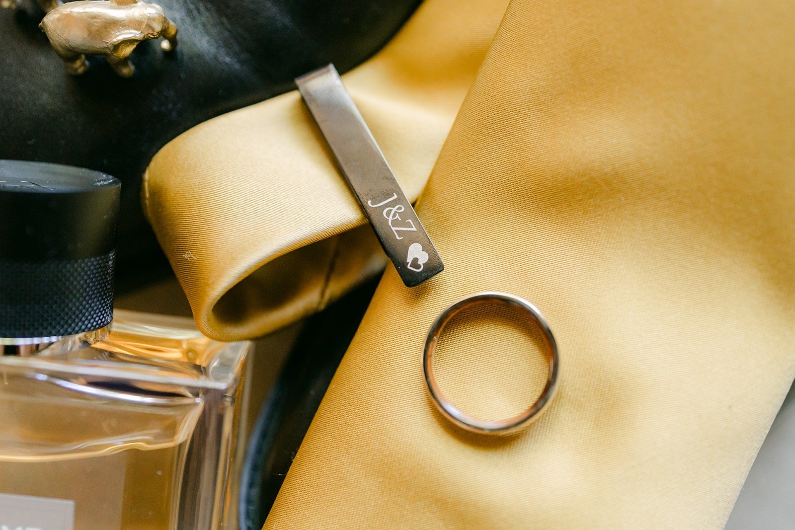 Zach's wedding band resting on a gold tie beside cufflinks, a tie bar and a cologne bottle