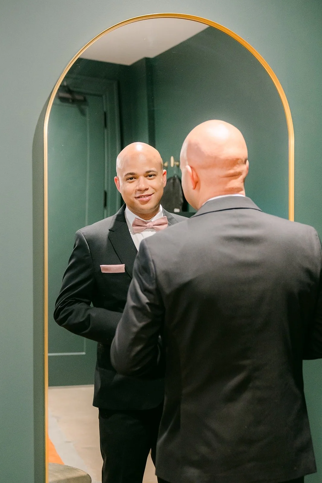Brandon gets help with his jacket in front of an arched mirror in The Vault at The Headquarters