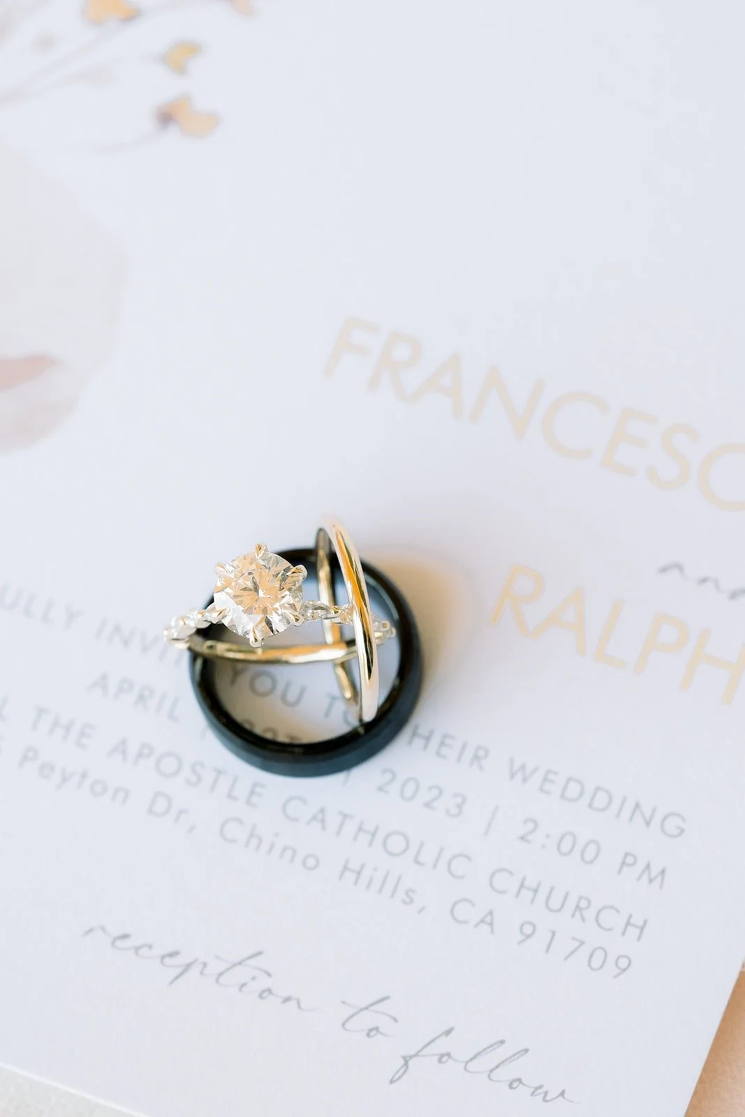 Engagement ring and wedding bands resting on the invitation naming St. Paul the Apostle Catholic Church in Chino Hills