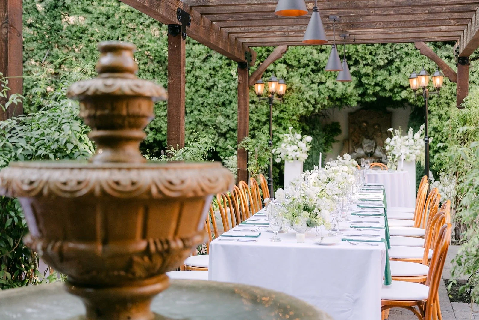 A stone fountain beside a long reception table at Franciscan Gardens