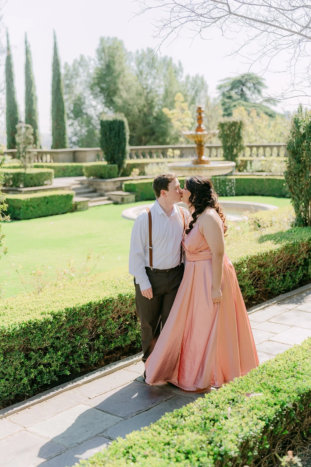 Saira and Matthew strolling the hedge-lined path toward the fountain.