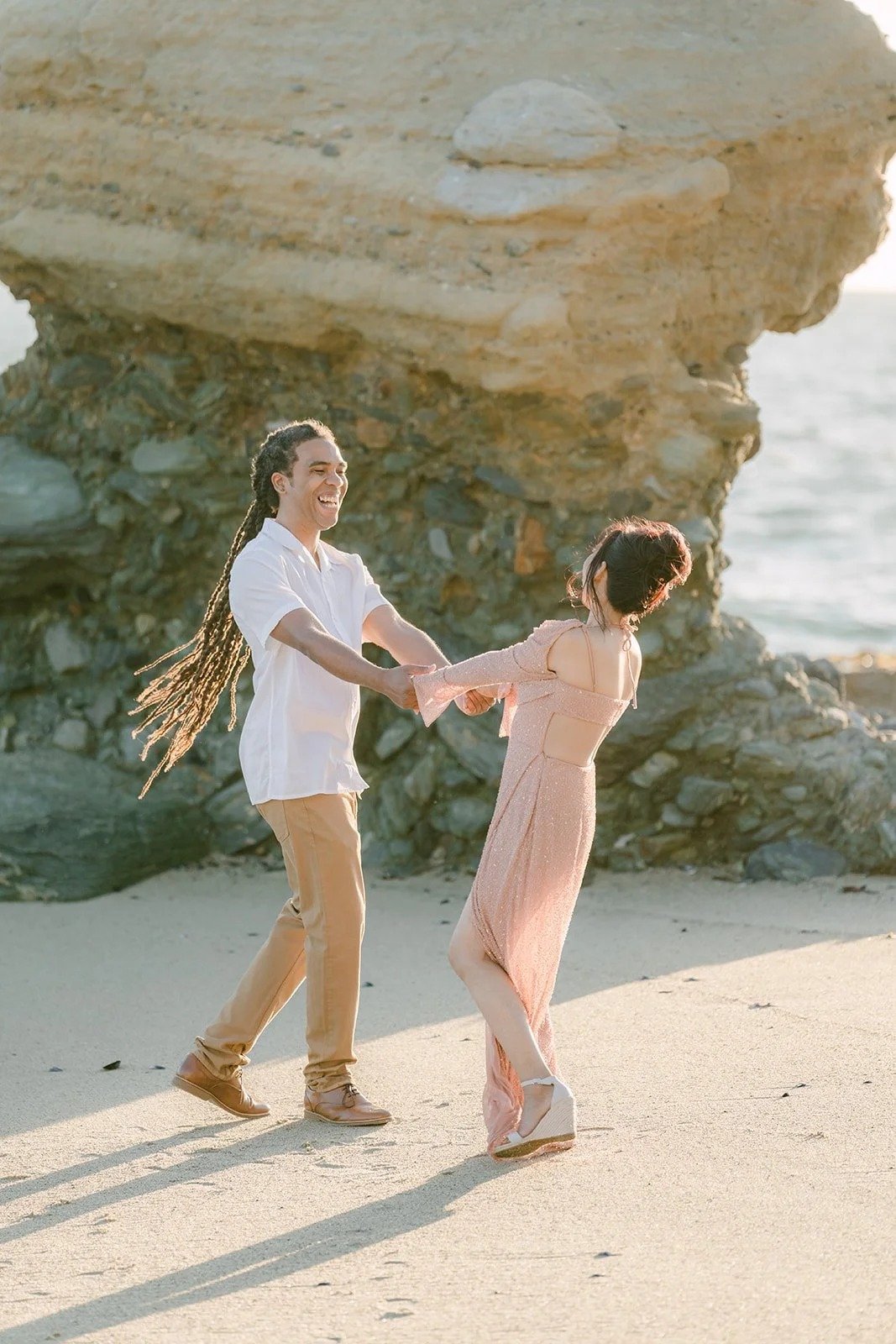 Amy in a pink gown twirling with Michael on the sand by Table Rock.
