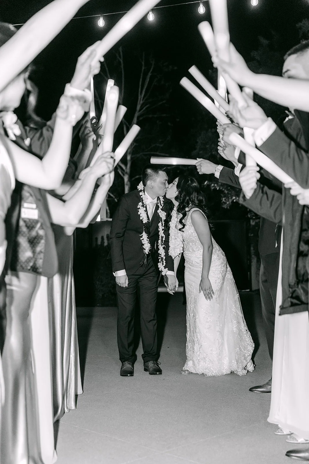 Kelli and Alex walking through a tunnel of light up foam sticks in black and white