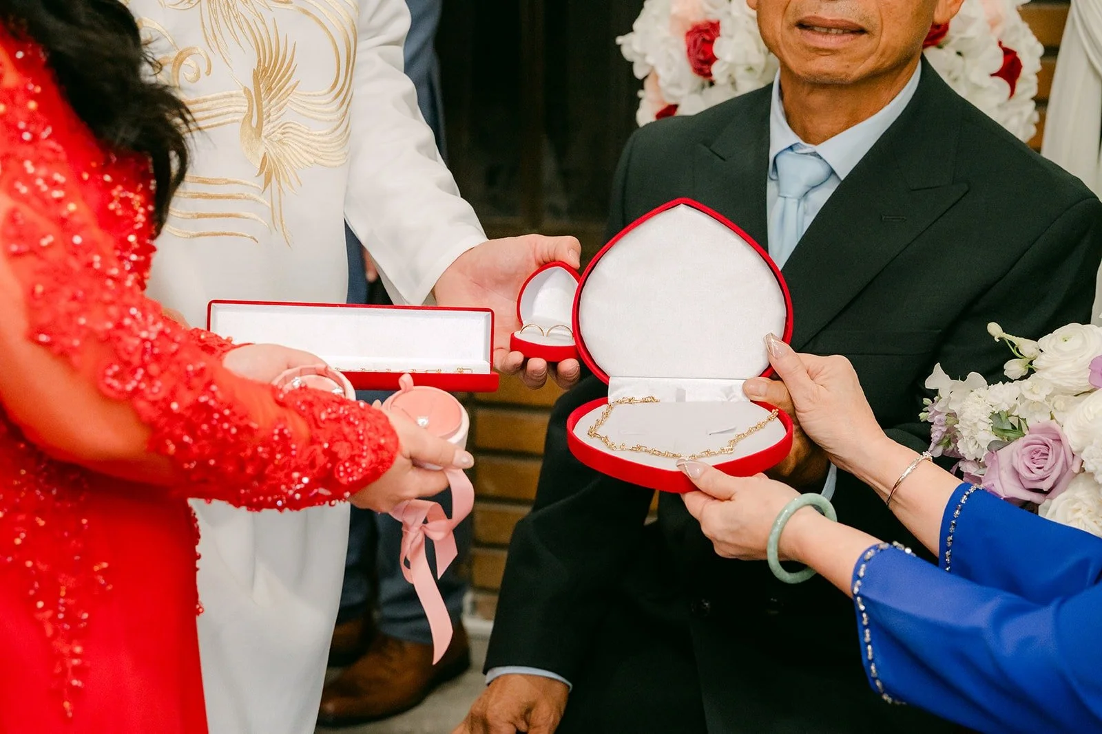 Family members open a red jewelry box to present a gift to the couple