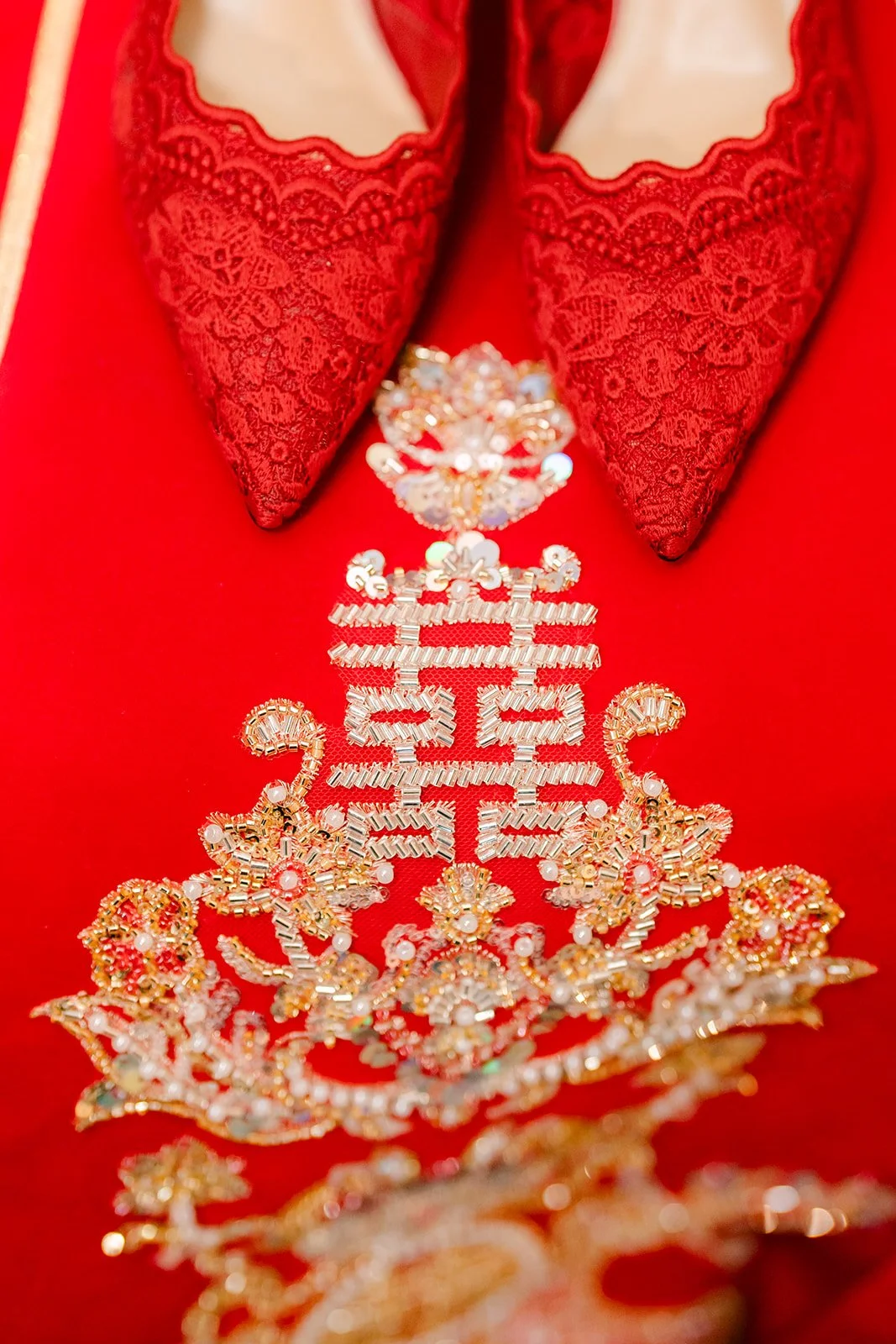 Red embroidered wedding shoes resting on a qun kwa with a gold double happiness design.