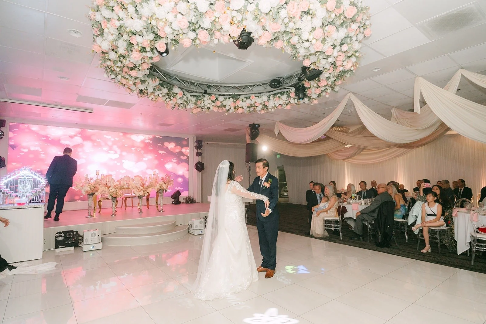 Parent dance under the floral chandelier as the room looks on