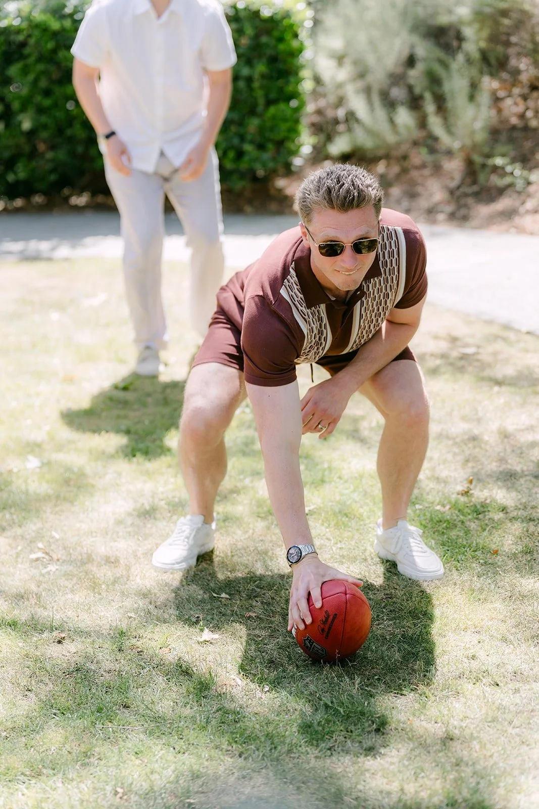 A groomsman crouched in a football stance over the ball on the grass