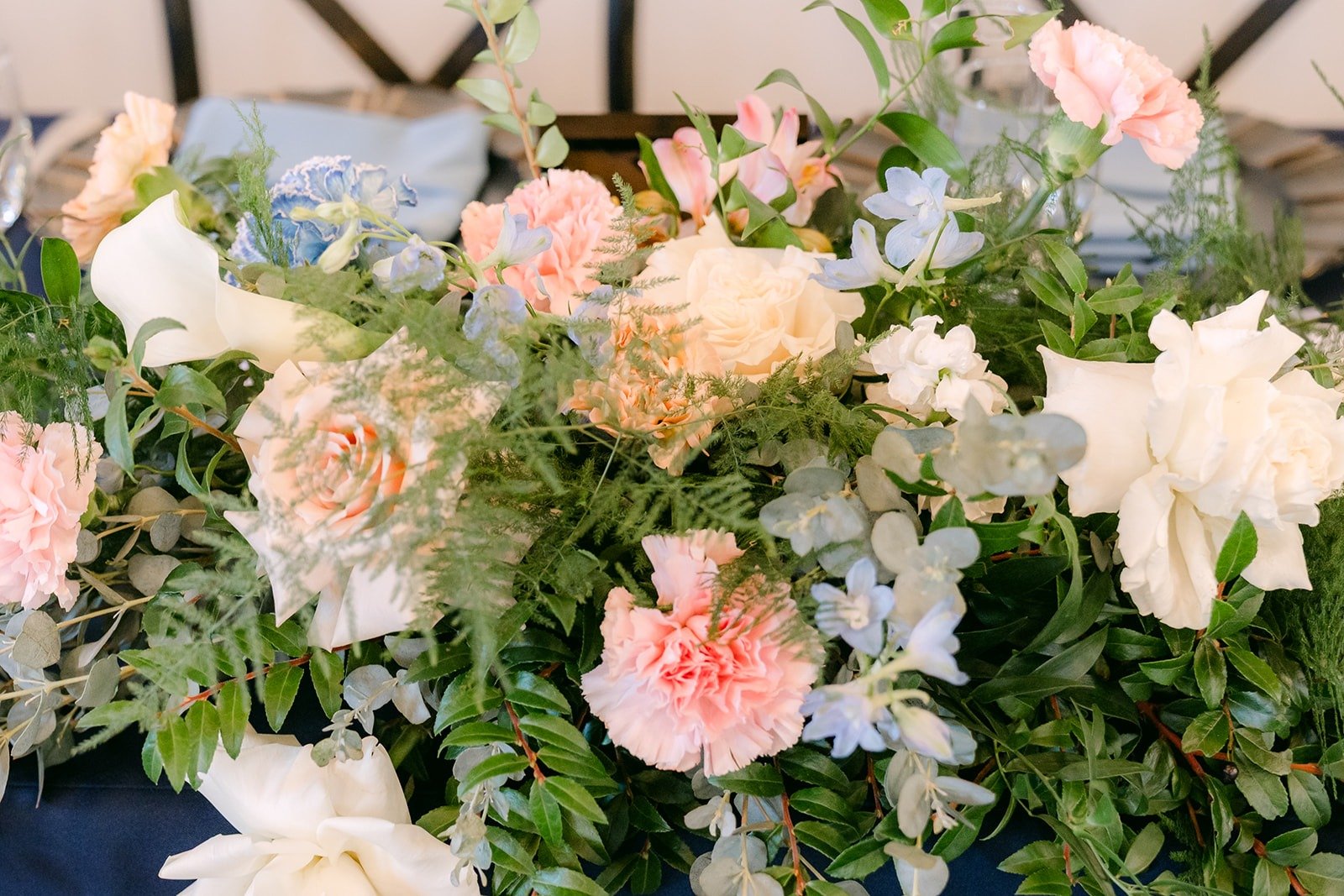 A centerpiece of blush, peach and white flowers with greenery