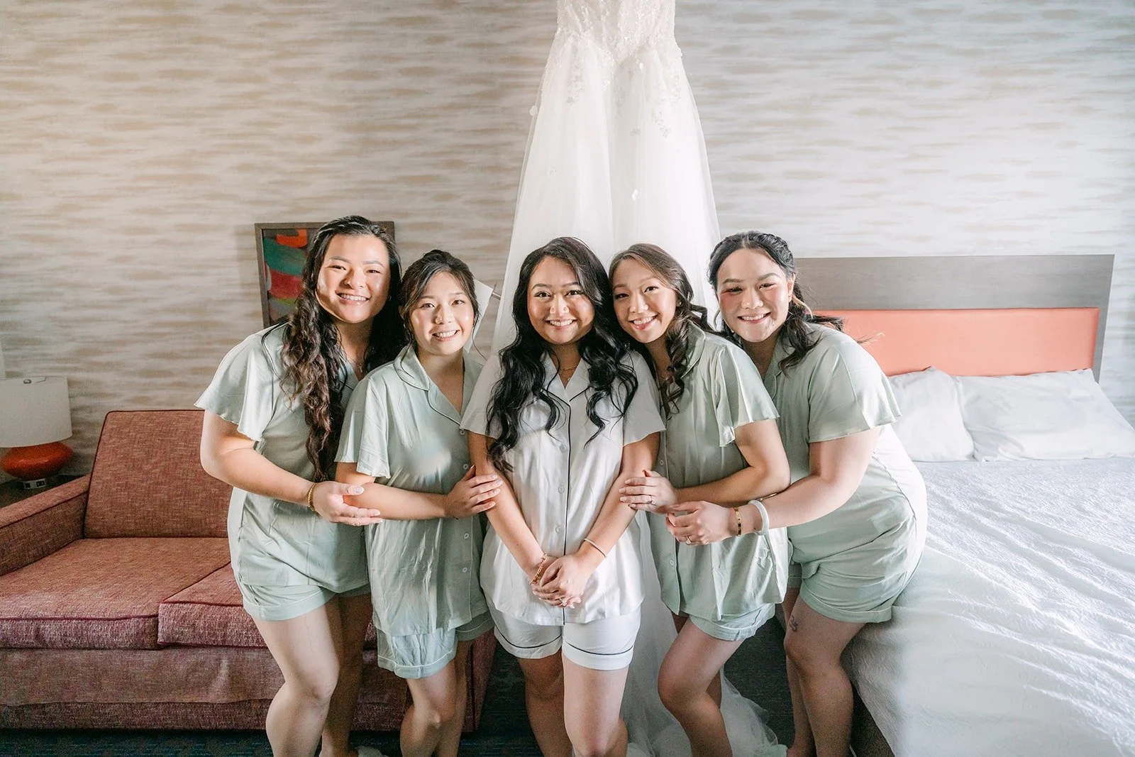 Jennifer and her bridesmaids in matching sage pajamas on the hotel bed