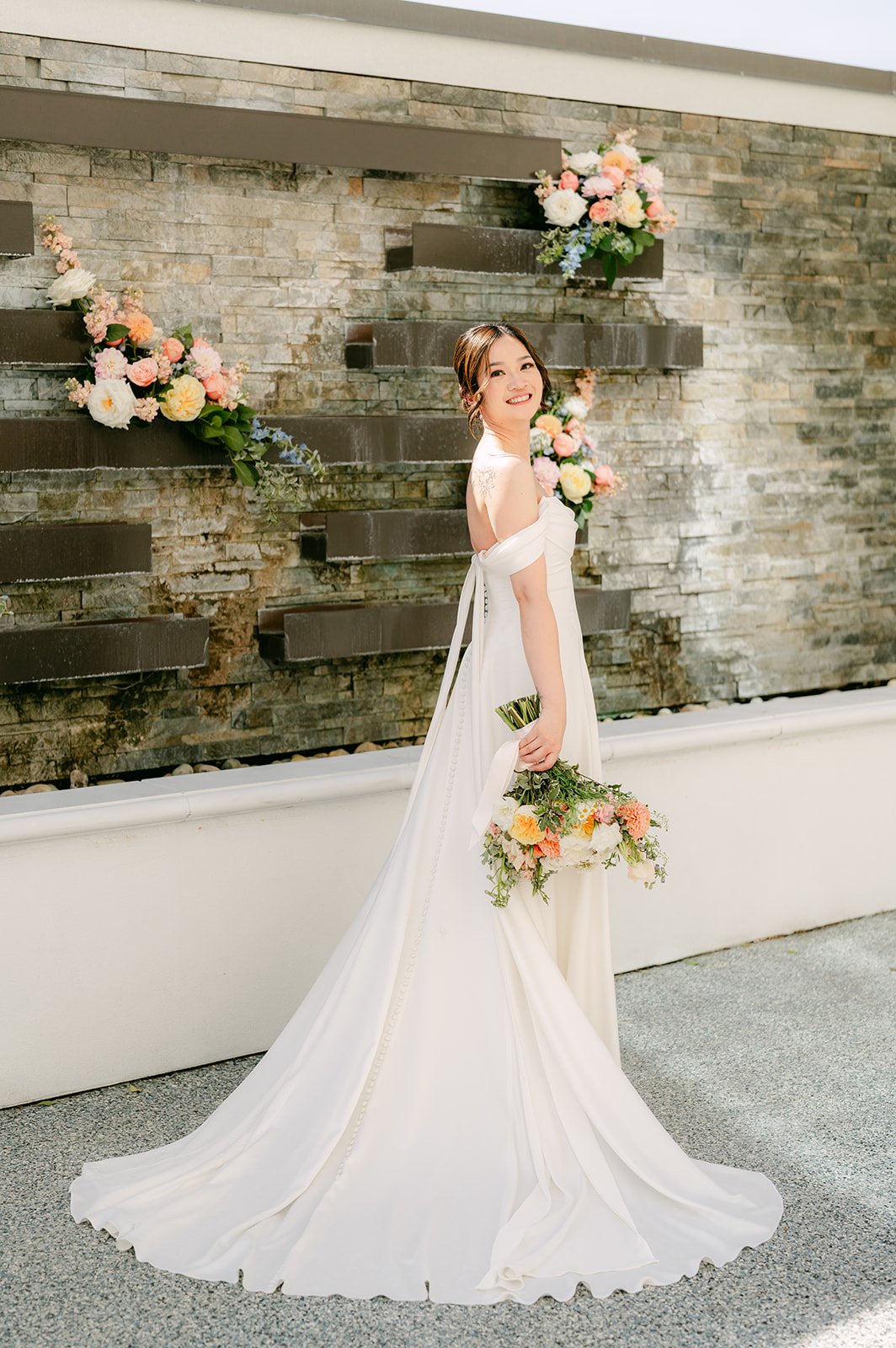 Amanda in her gown with a long train beside the stone wall.