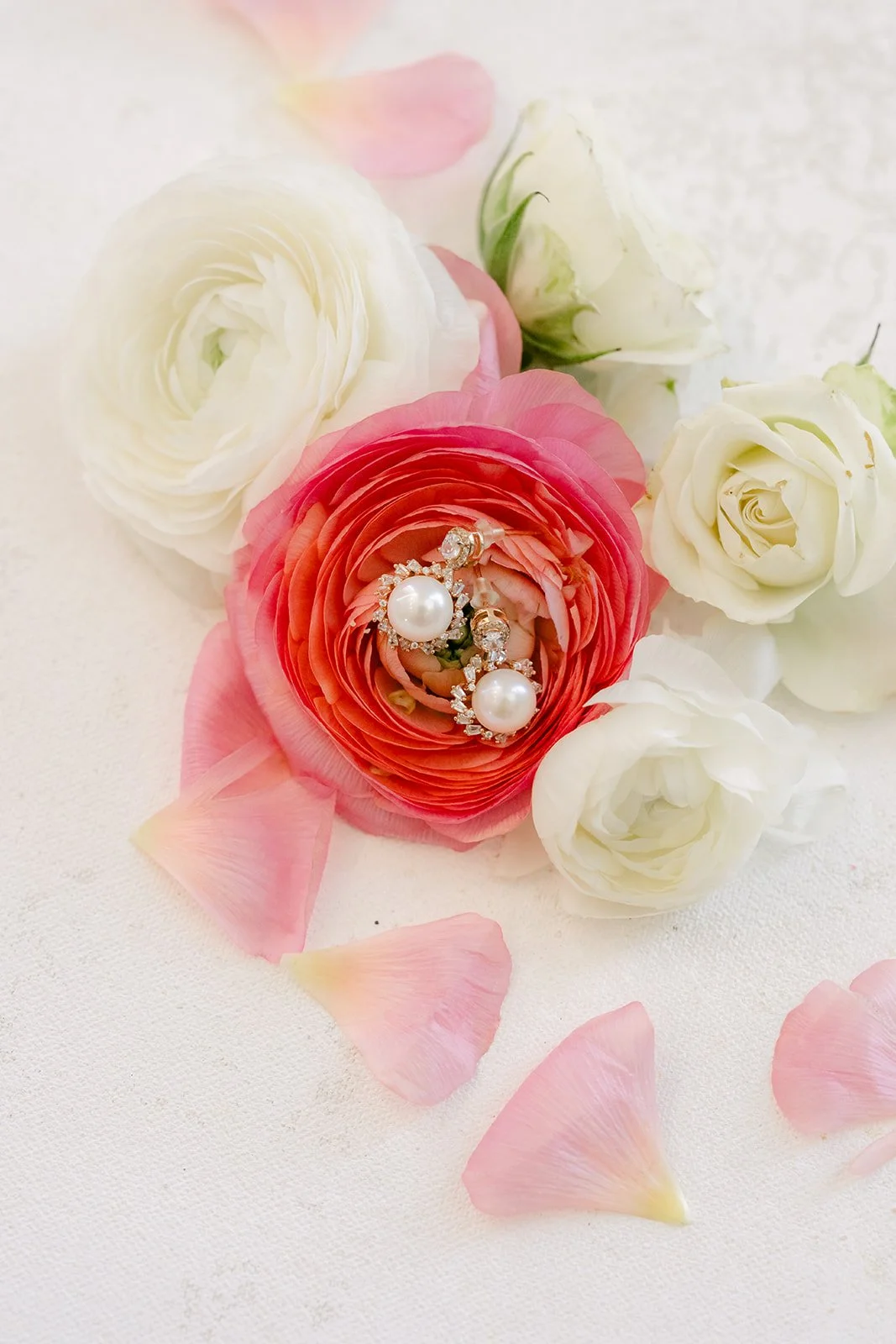 Pearl earrings resting on pink ranunculus and white roses