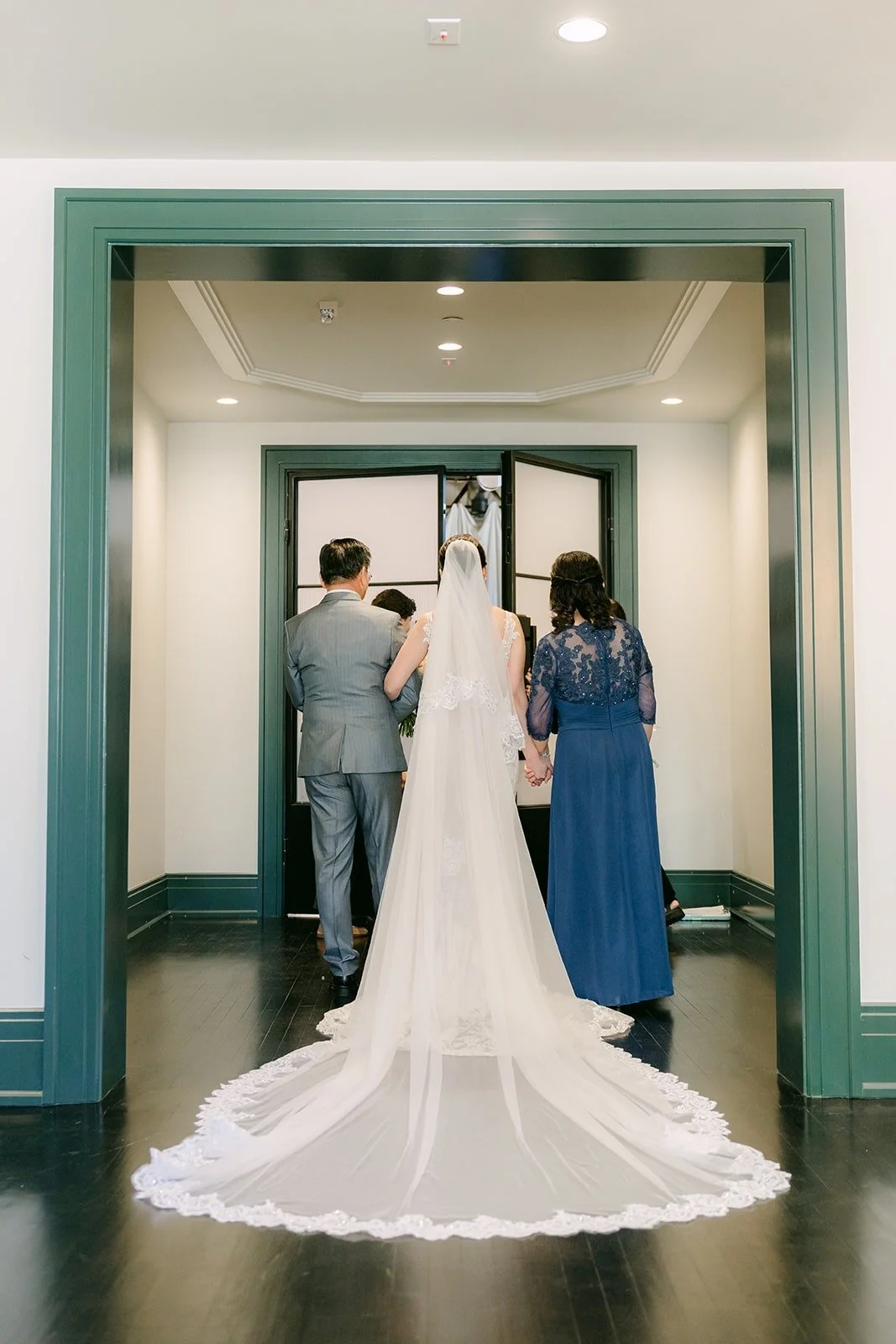 Elisa walks toward the ceremony with her parents, her long train behind her
