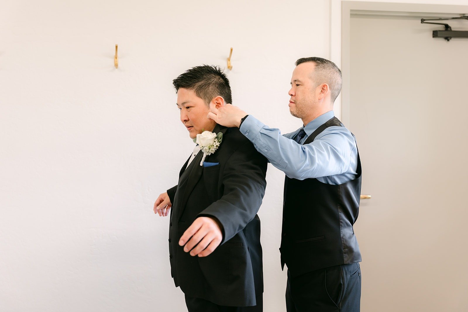 A groomsman helps Jay into his tuxedo jacket