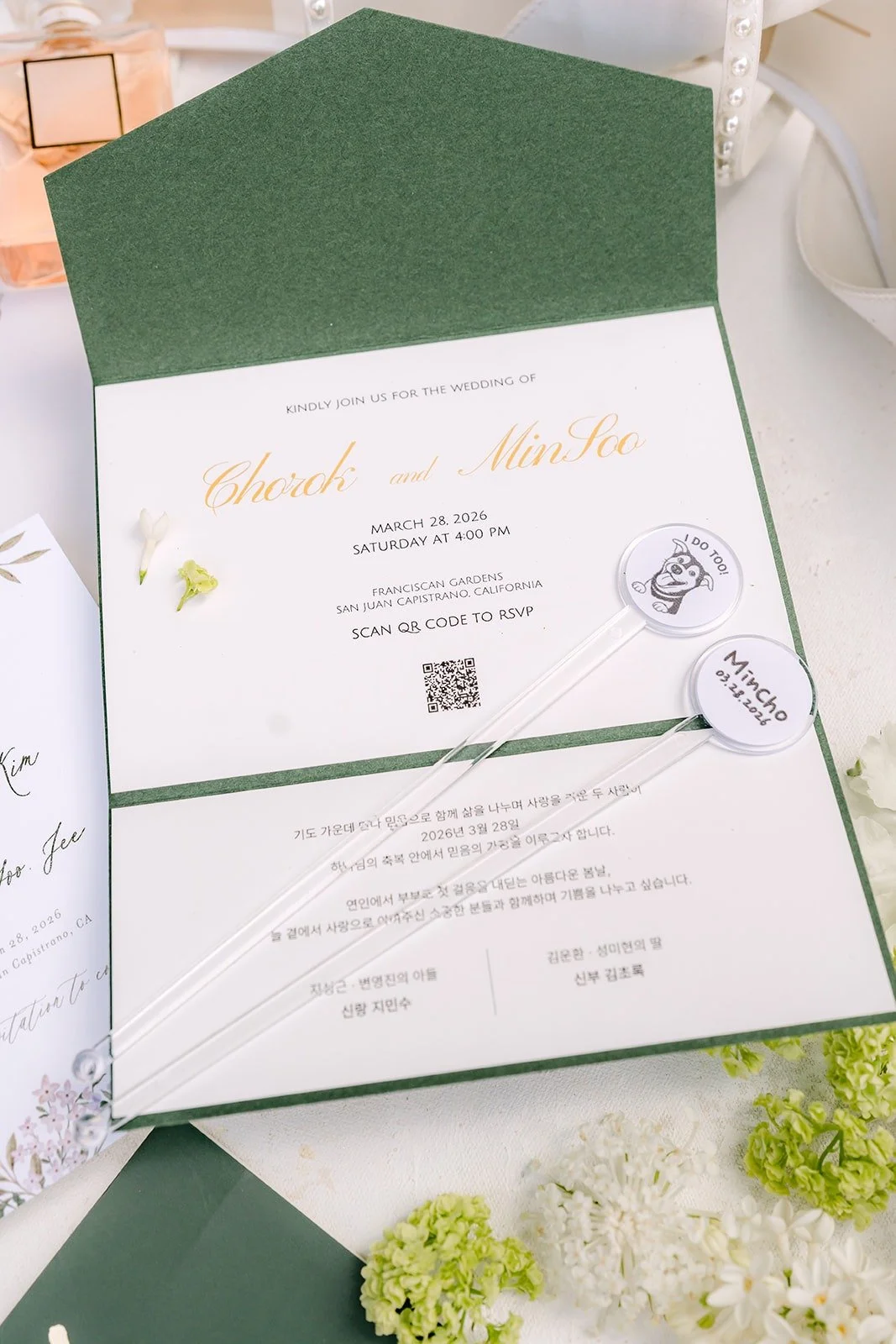 A green and white wedding invitation laid out with fresh white flowers