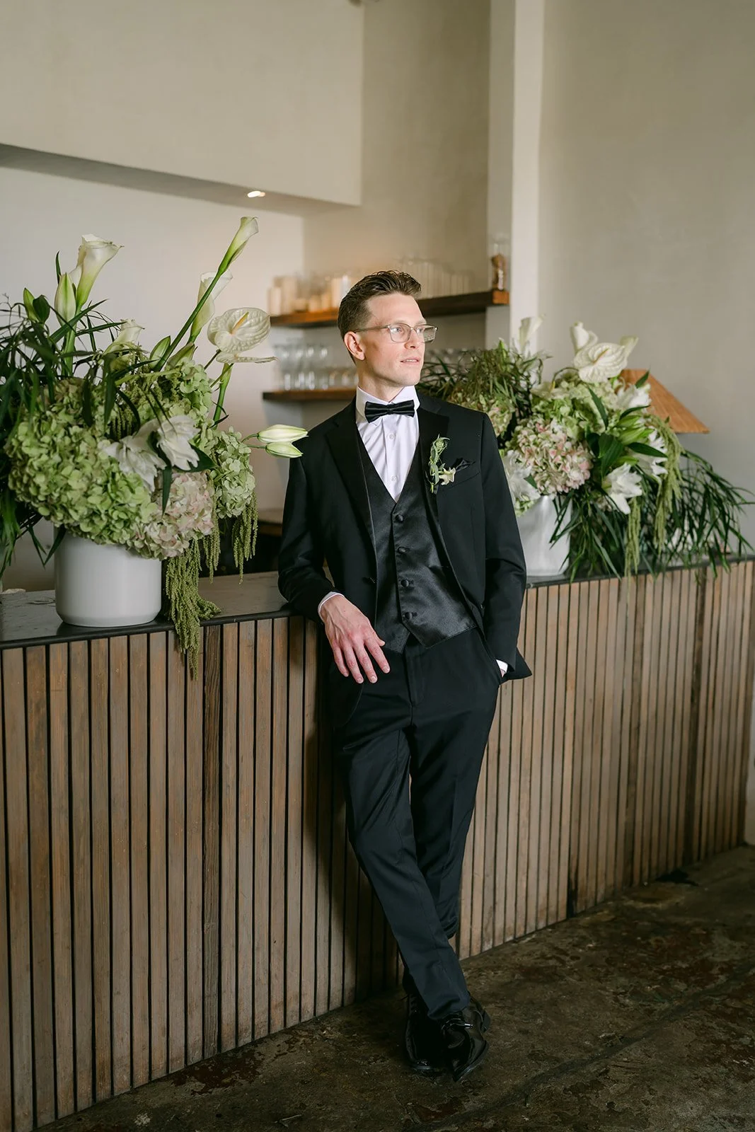Matthew leaning against the bar in his tuxedo