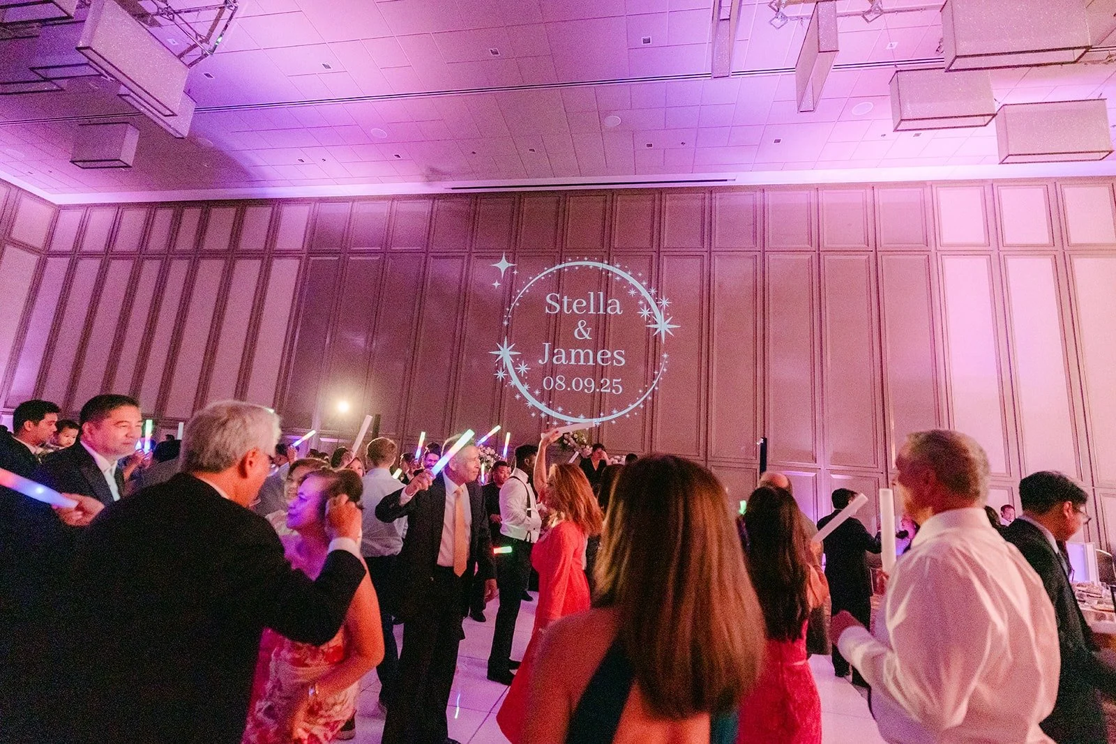 Guests dancing under purple lights with the couple's monogram on the wall