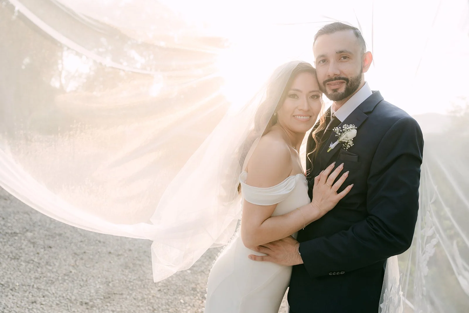 Couple in backlit afternoon sun with her veil floating behind them