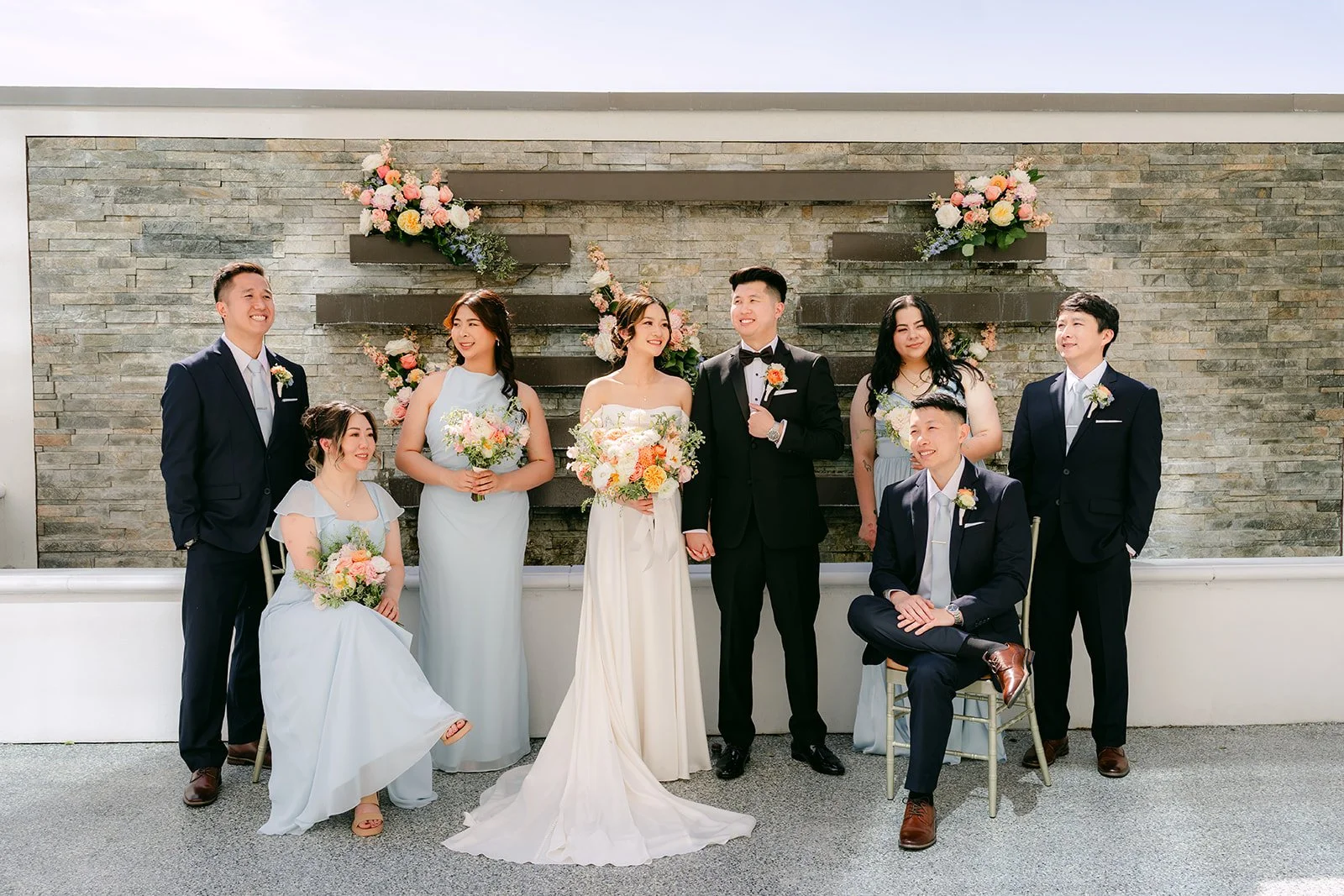 Amanda and San with their wedding party in front of the stone wall.