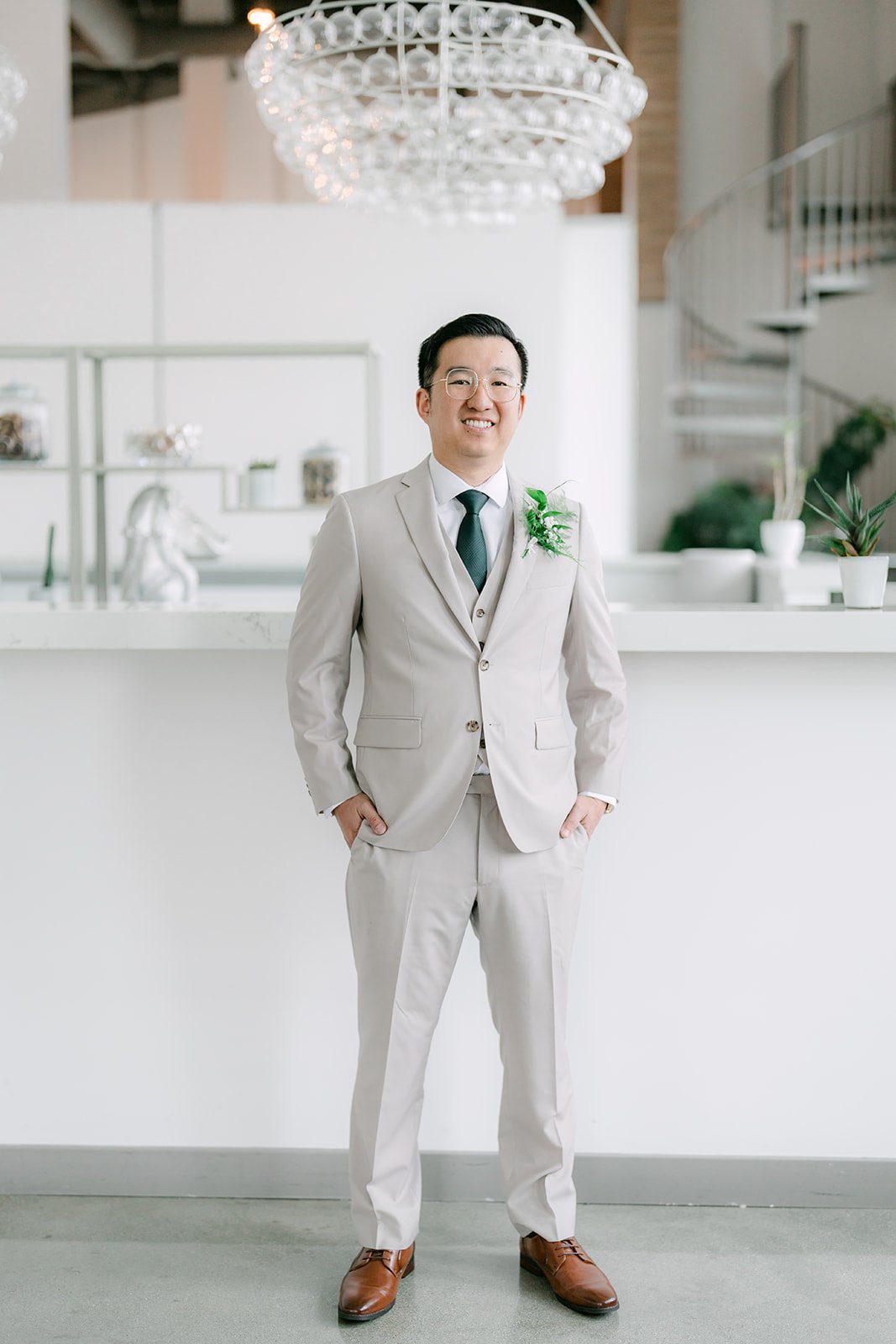 Ricky in a tan suit and emerald tie standing in the groom's suite