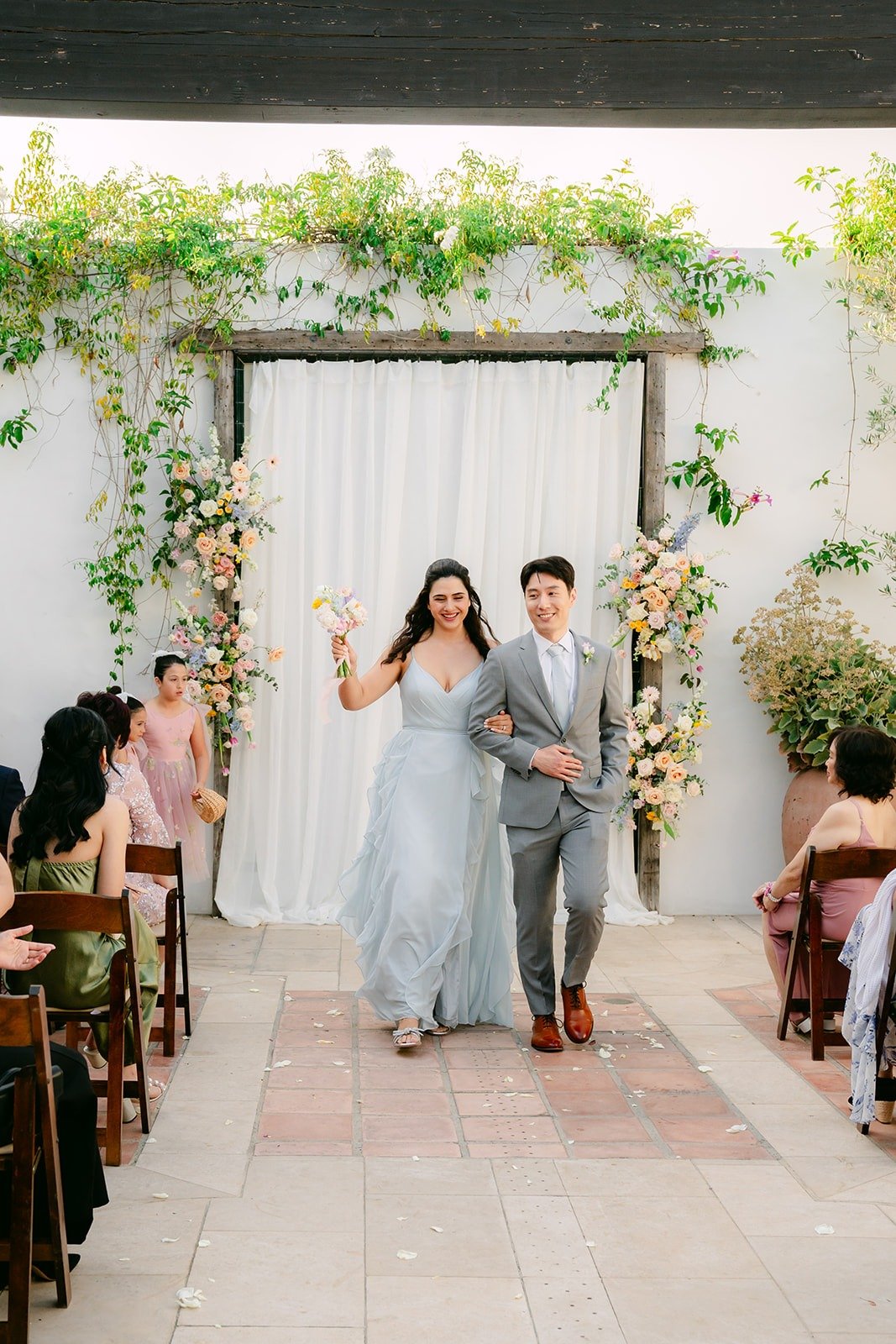A bridesmaid and groomsman walking in together under the greenery arch