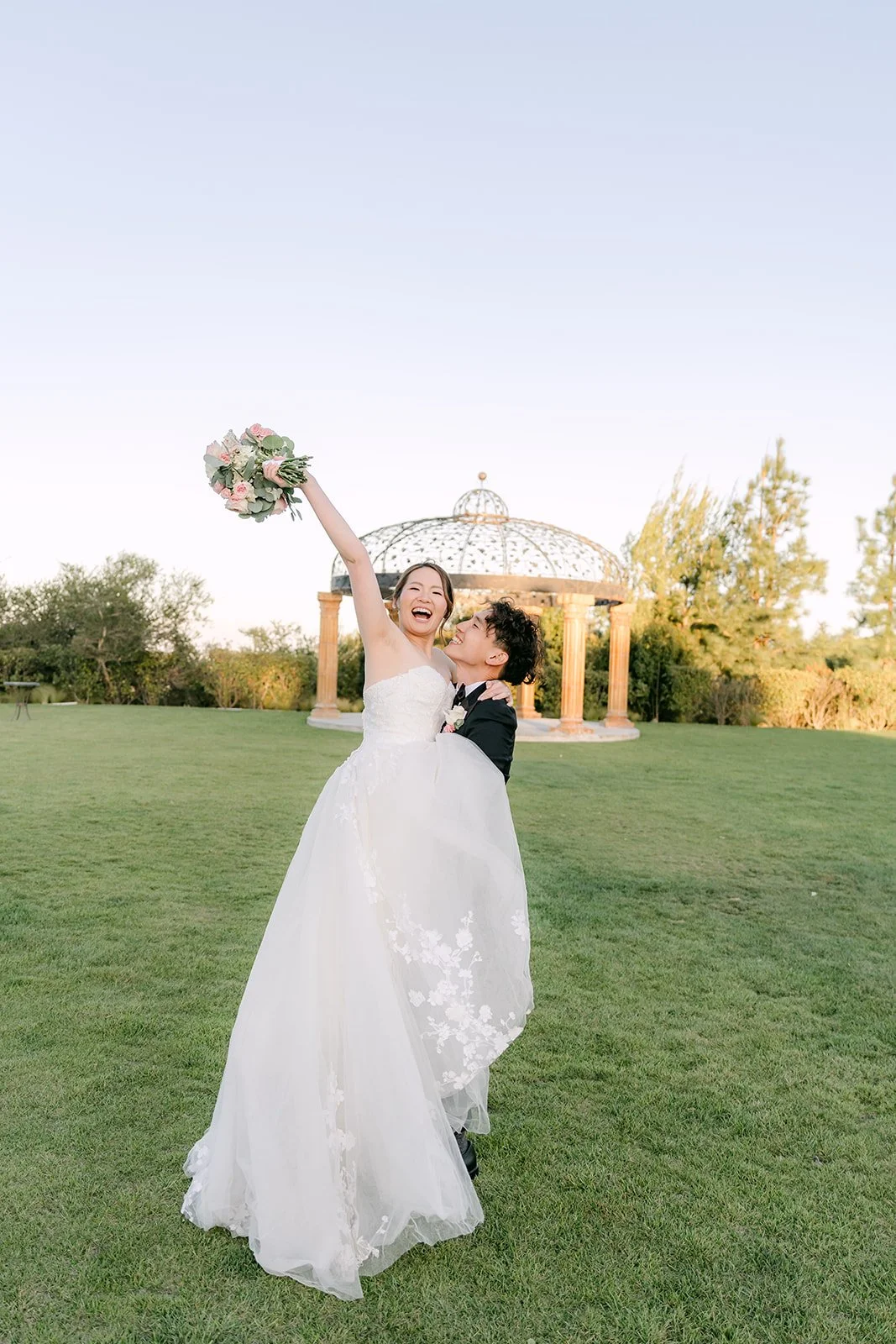 Bride raising her bouquet in celebration on the lawn
