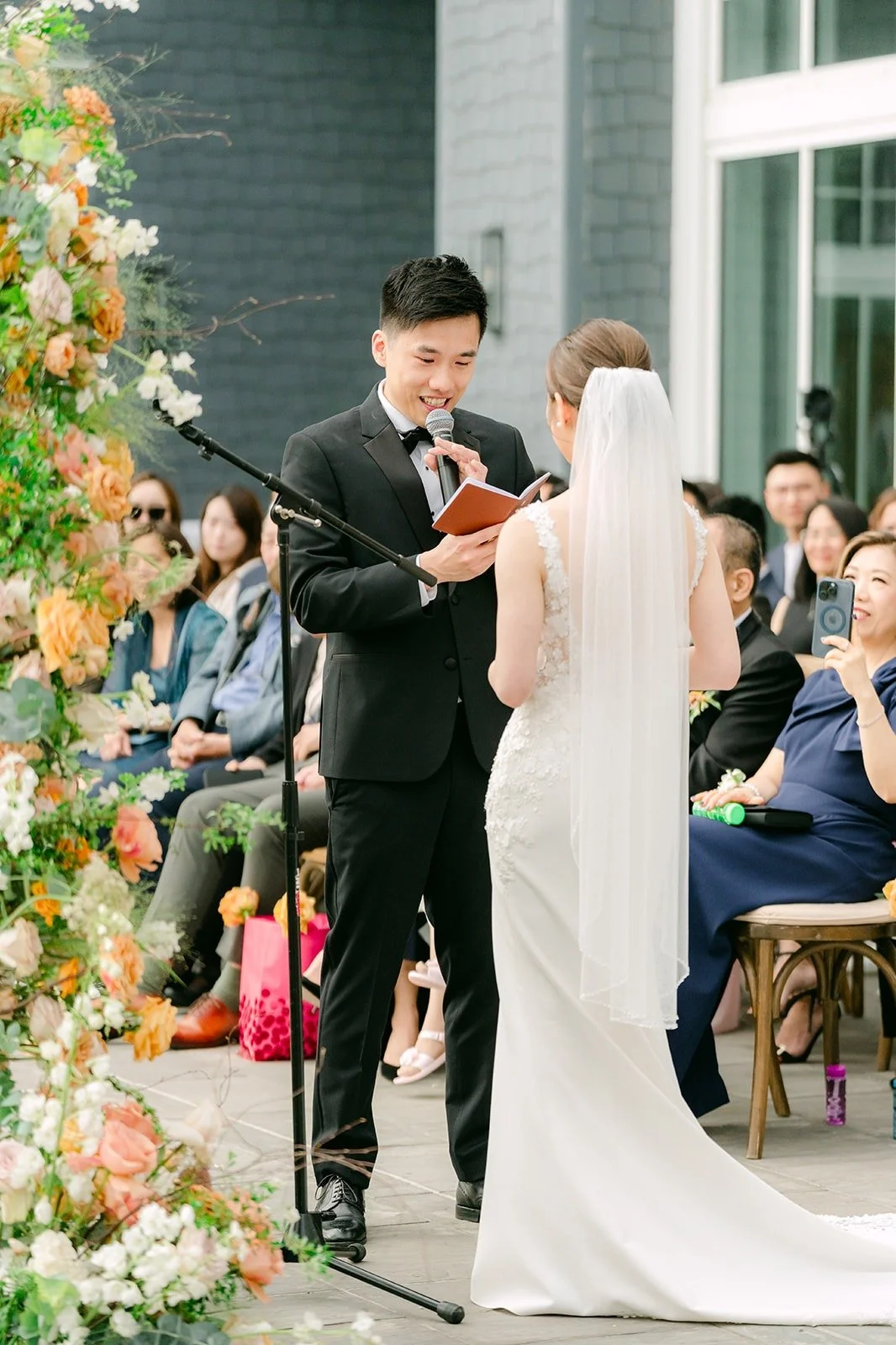 Eli and Angela holding hands at the floral arch as Eli speaks