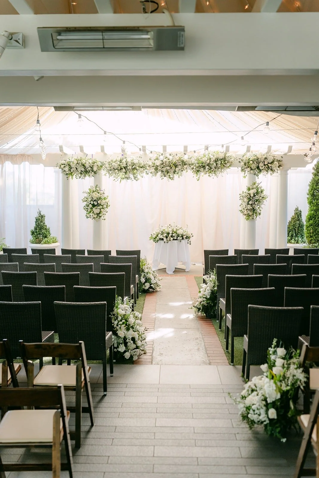 Ceremony chairs facing a white draped backdrop with greenery and white flowers at Five Crowns