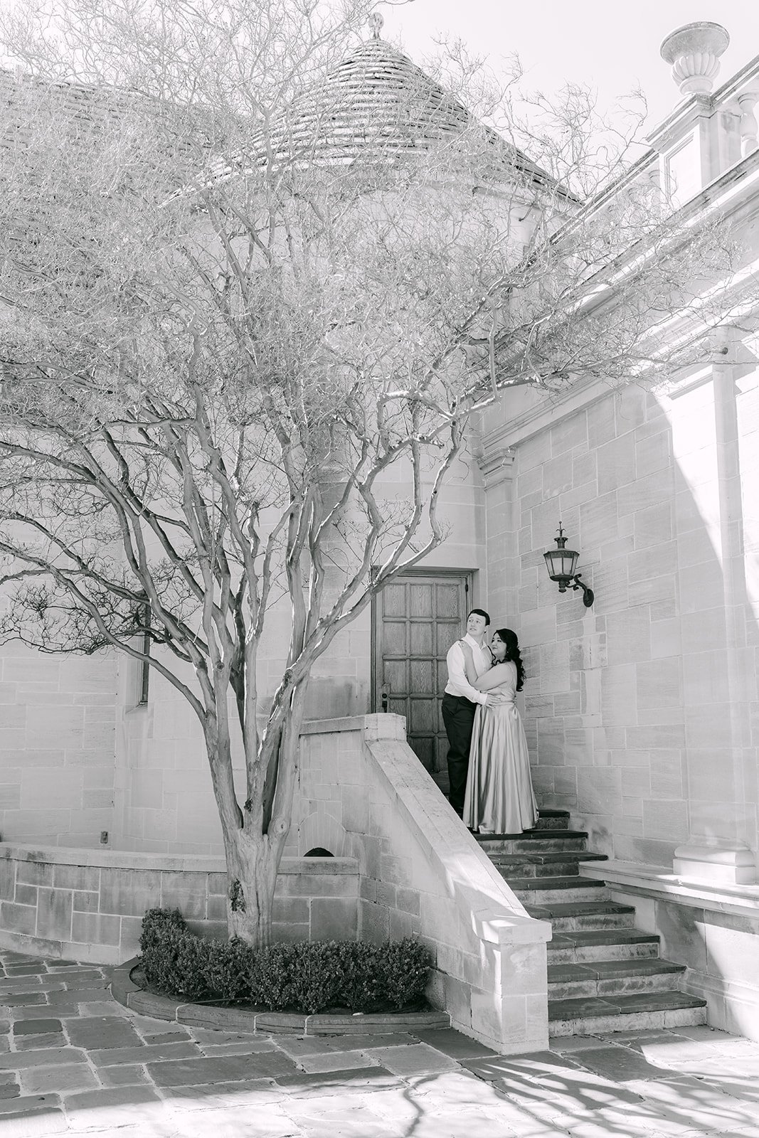 Black and white portrait of Saira and Matthew on the courtyard steps of the mansion.
