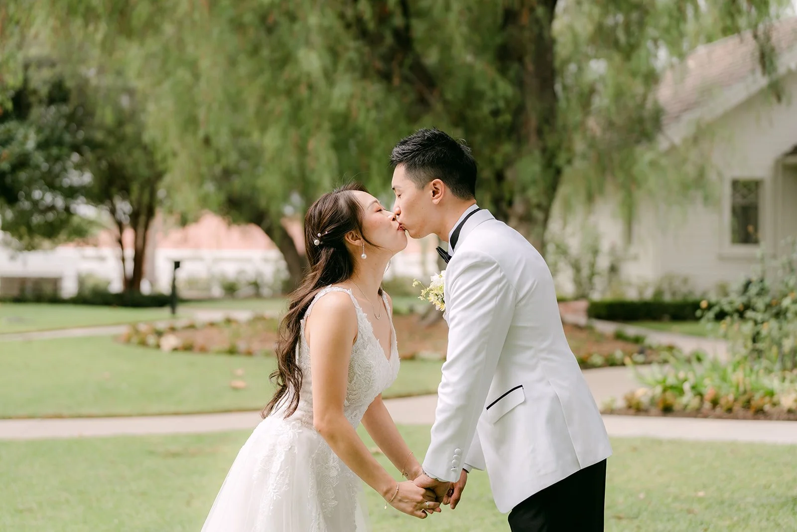 Jenny and Ryan sharing a kiss on the lawn under the trees.