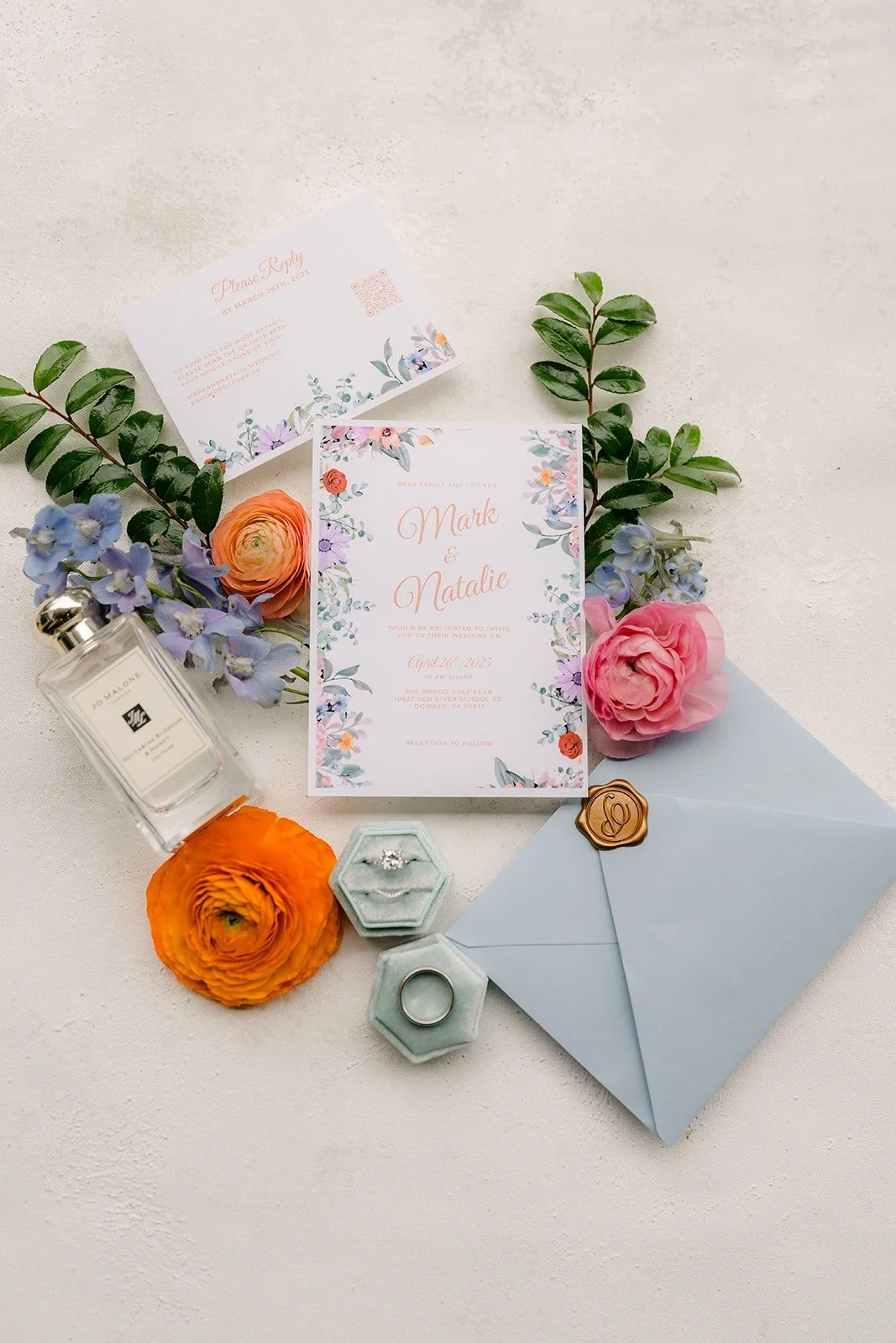 Natalie and Mark's wedding invitation suite styled with dusty blue envelopes, a perfume bottle and peach and pink blooms